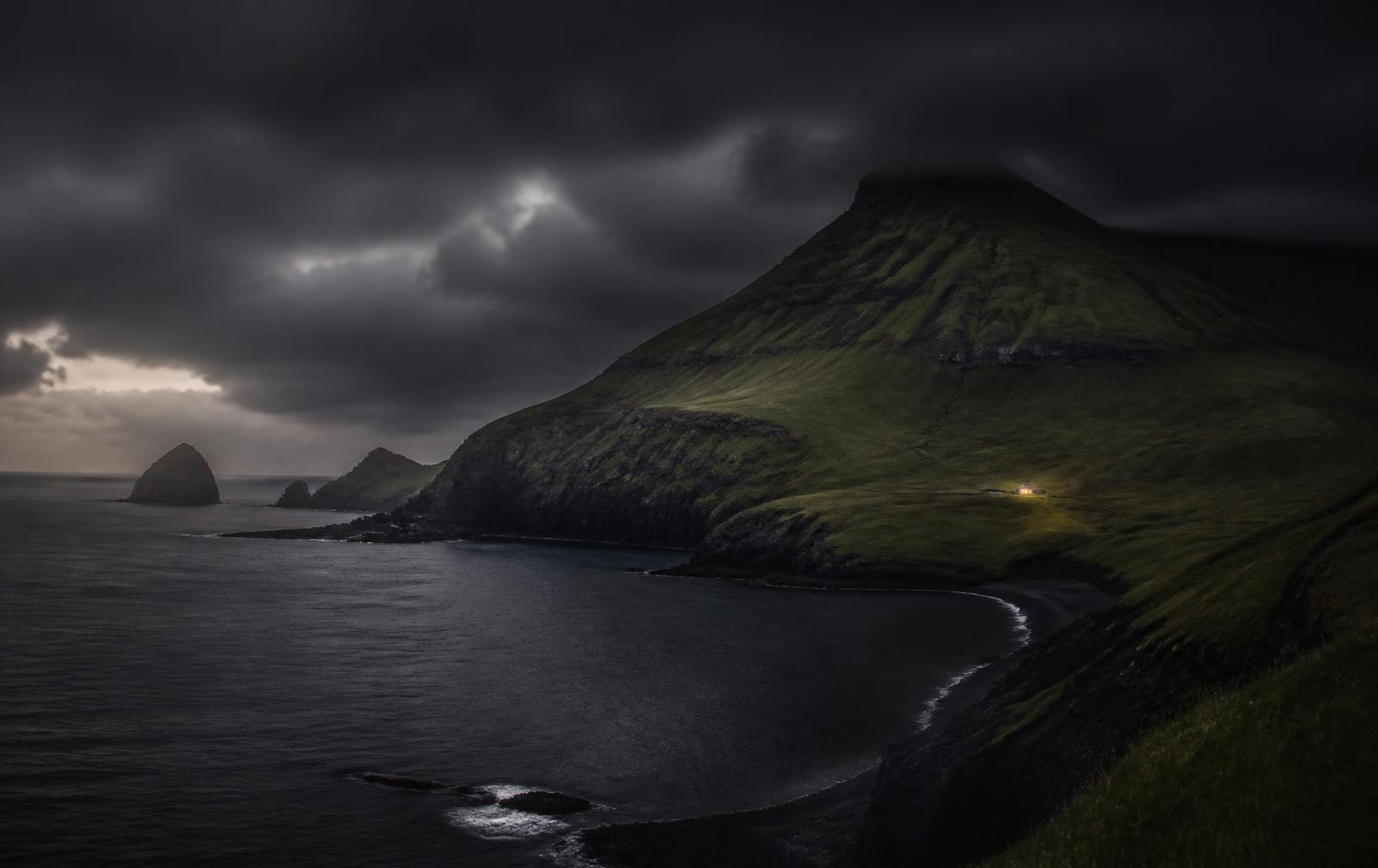 A remote green volcanic coastline under heavy dark Atlantic cloud at dusk