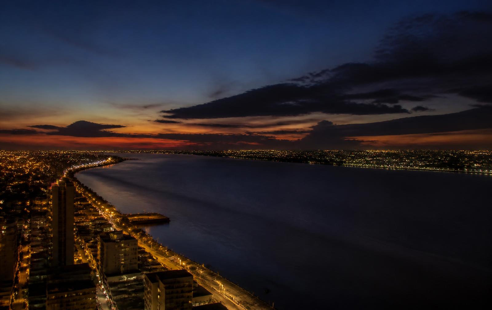 Barranquilla at dusk, city lights along the dark Magdalena river under a deep evening sky