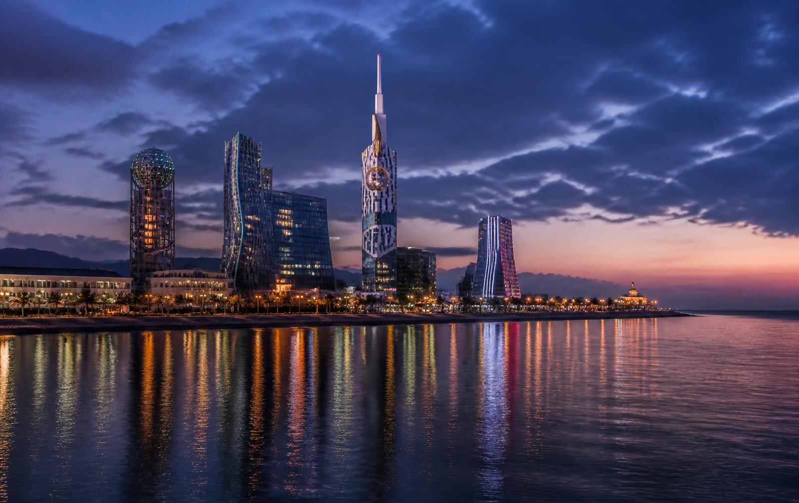 Batumi waterfront at dusk, modern towers and promenade lights reflected in the dark Black Sea