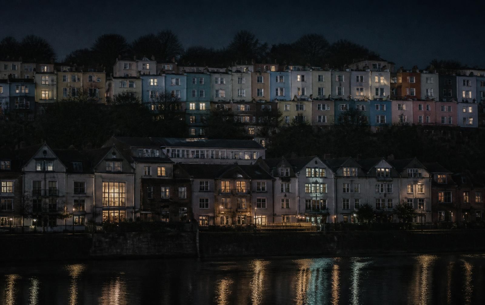 Bristol terraces on the hill at night above dark harbour water with warm lit windows