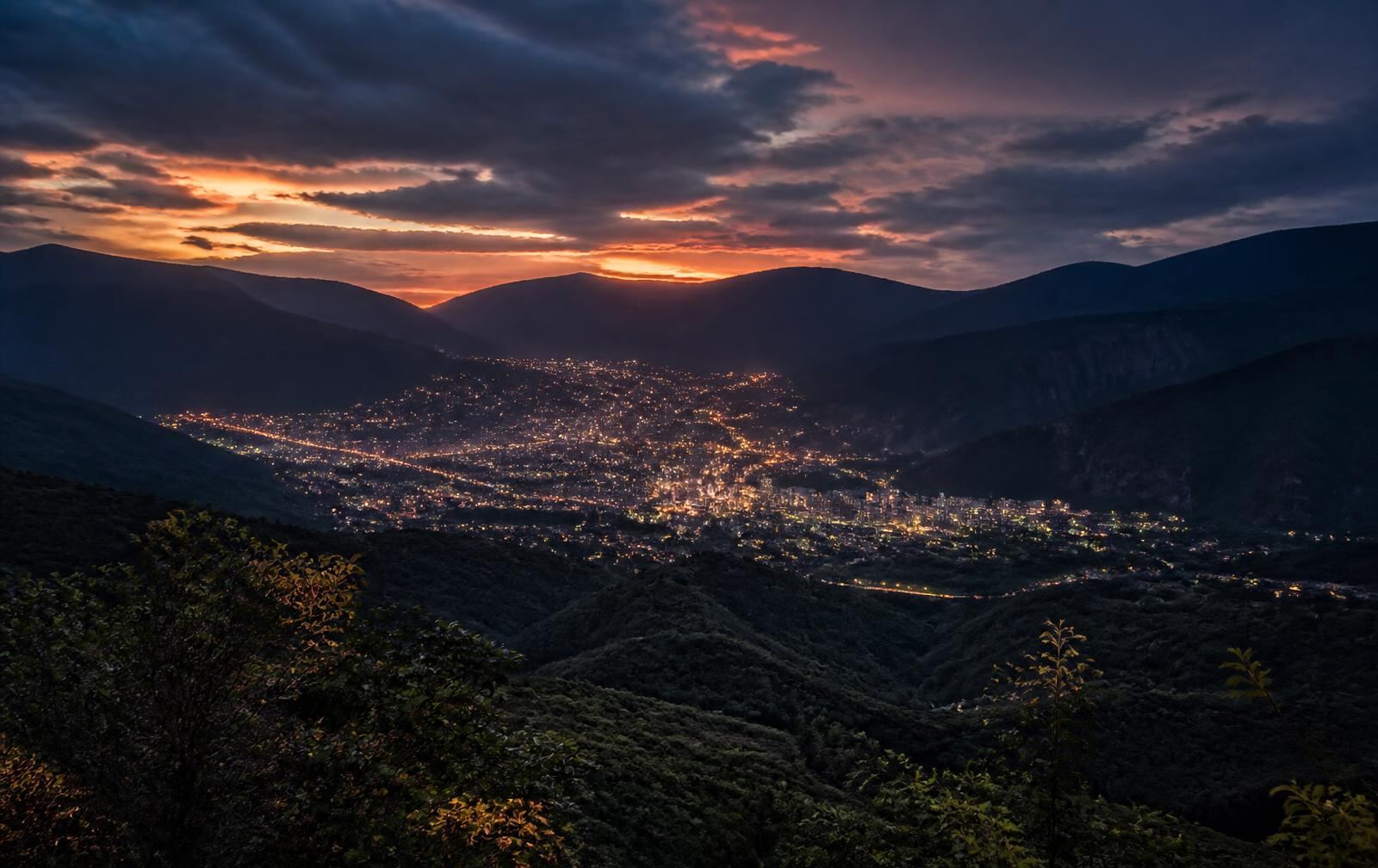 Bucaramanga at dusk, city lights gathered in a green mountain valley under a dramatic evening sky