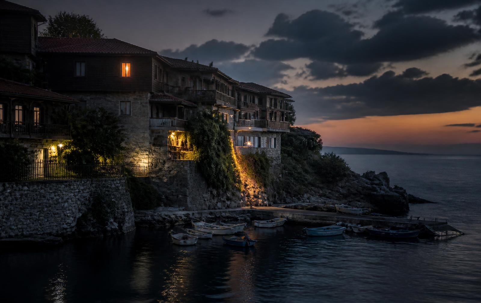 Sozopol's old stone and timber houses above the harbour at dusk, one window glowing warm