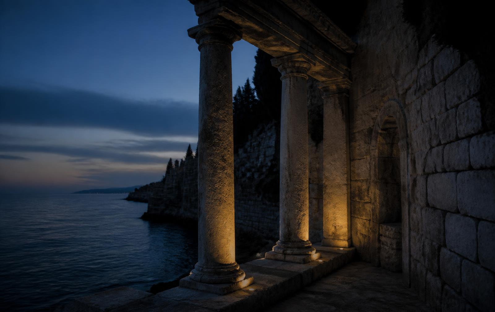 Ancient stone columns and a ruined coastal wall beside a dark Mediterranean sea at blue hour
