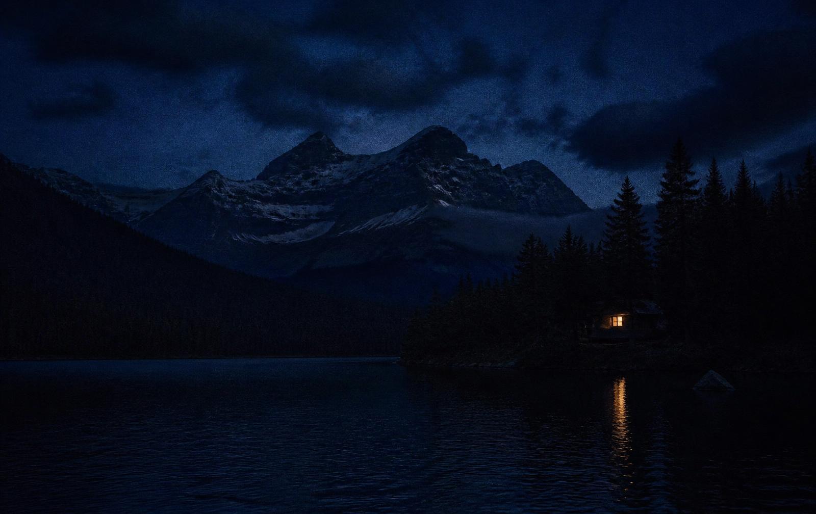 Dark Canadian lake and mountains at night with a single warm light on the far shore