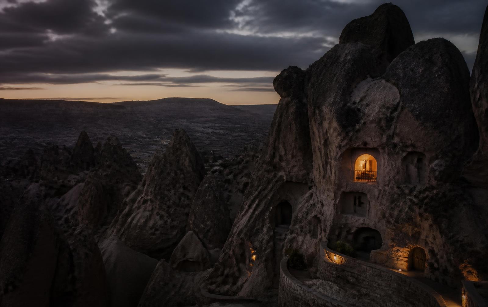 Cappadocian rock valleys before dawn in deep shadow with one warmly lit carved window
