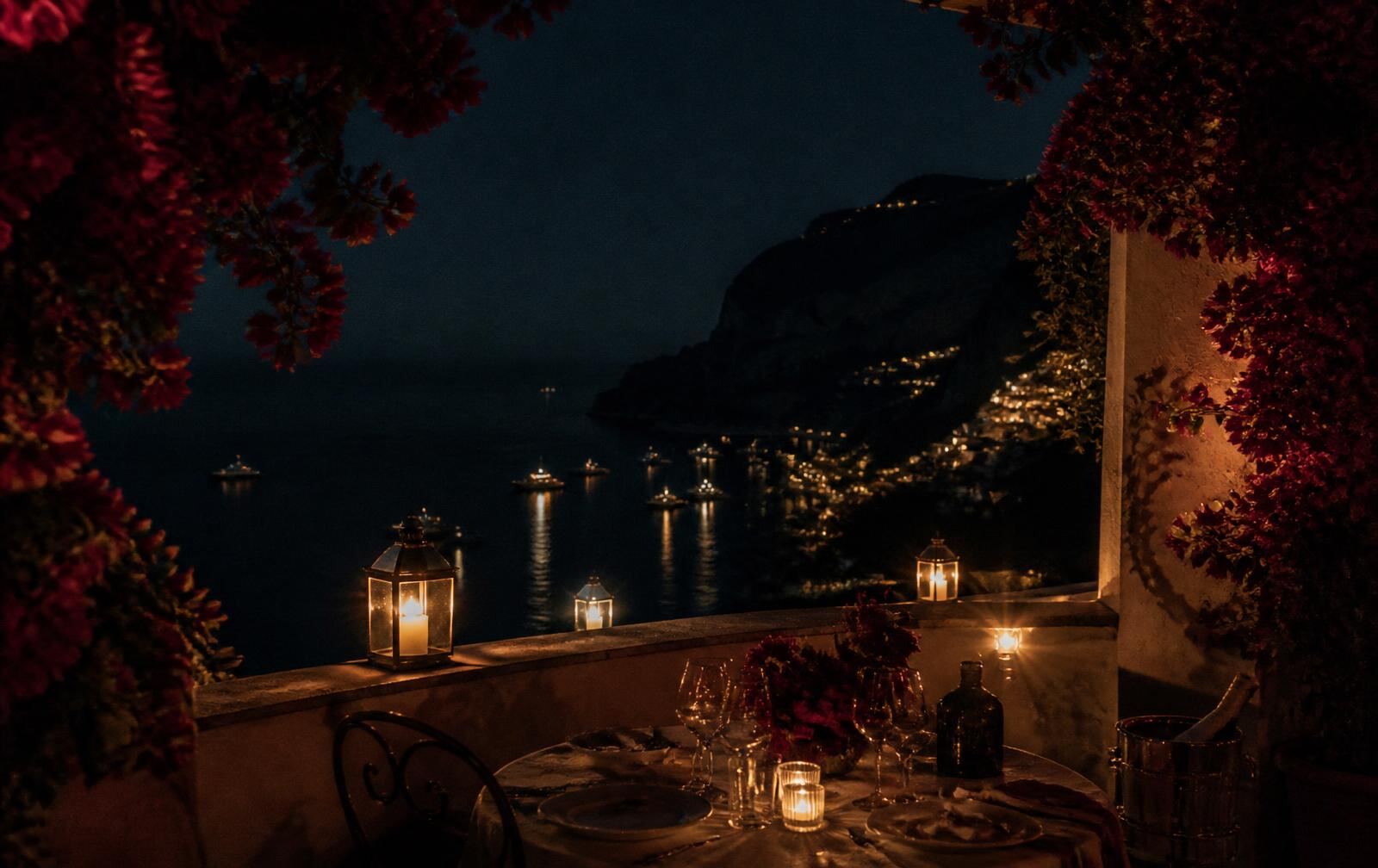 A bougainvillea-framed Capri terrace at night with lanterns above the dark Mediterranean and distant boat lights