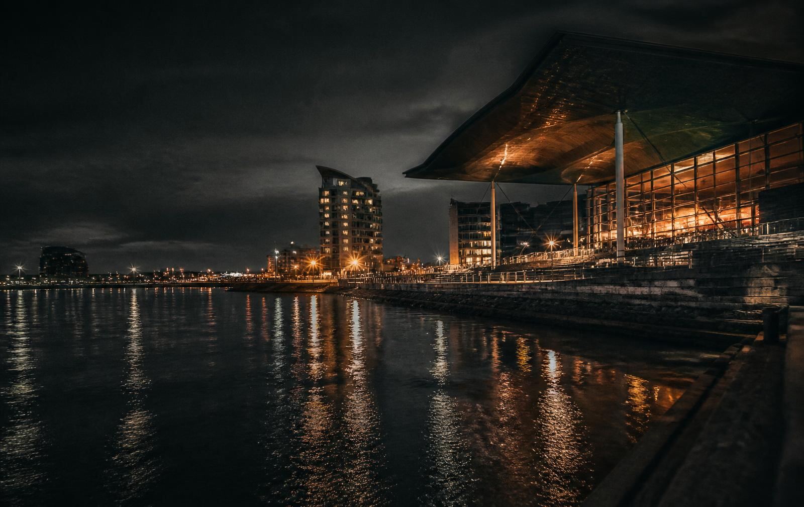 Cardiff Bay waterfront at night with dark water and warm light from modern architecture