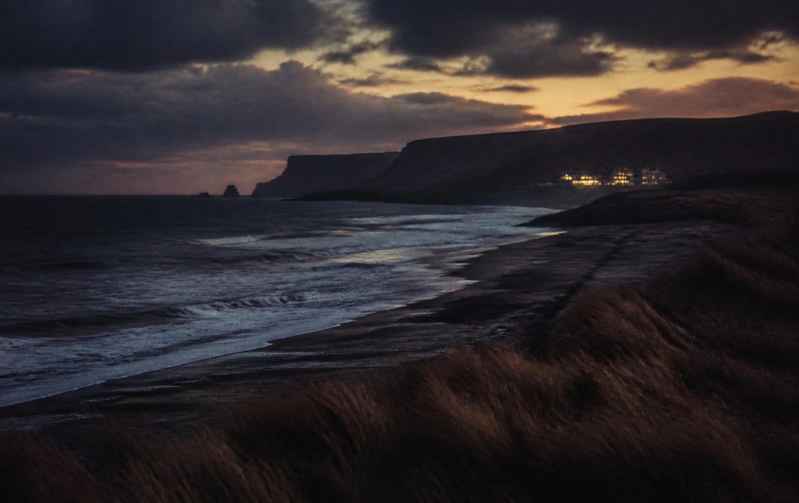 North Antrim coast at dusk with dark Atlantic surf, cliffs and a distant lit hotel above the dunes