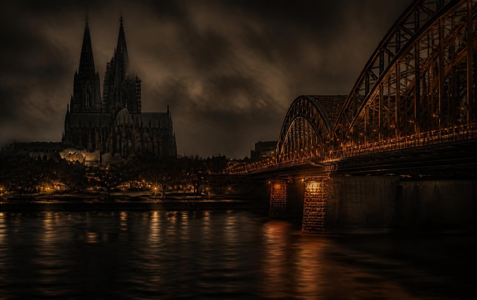 Cologne at night with the cathedral silhouette above old stone streets and warm light on the Rhine