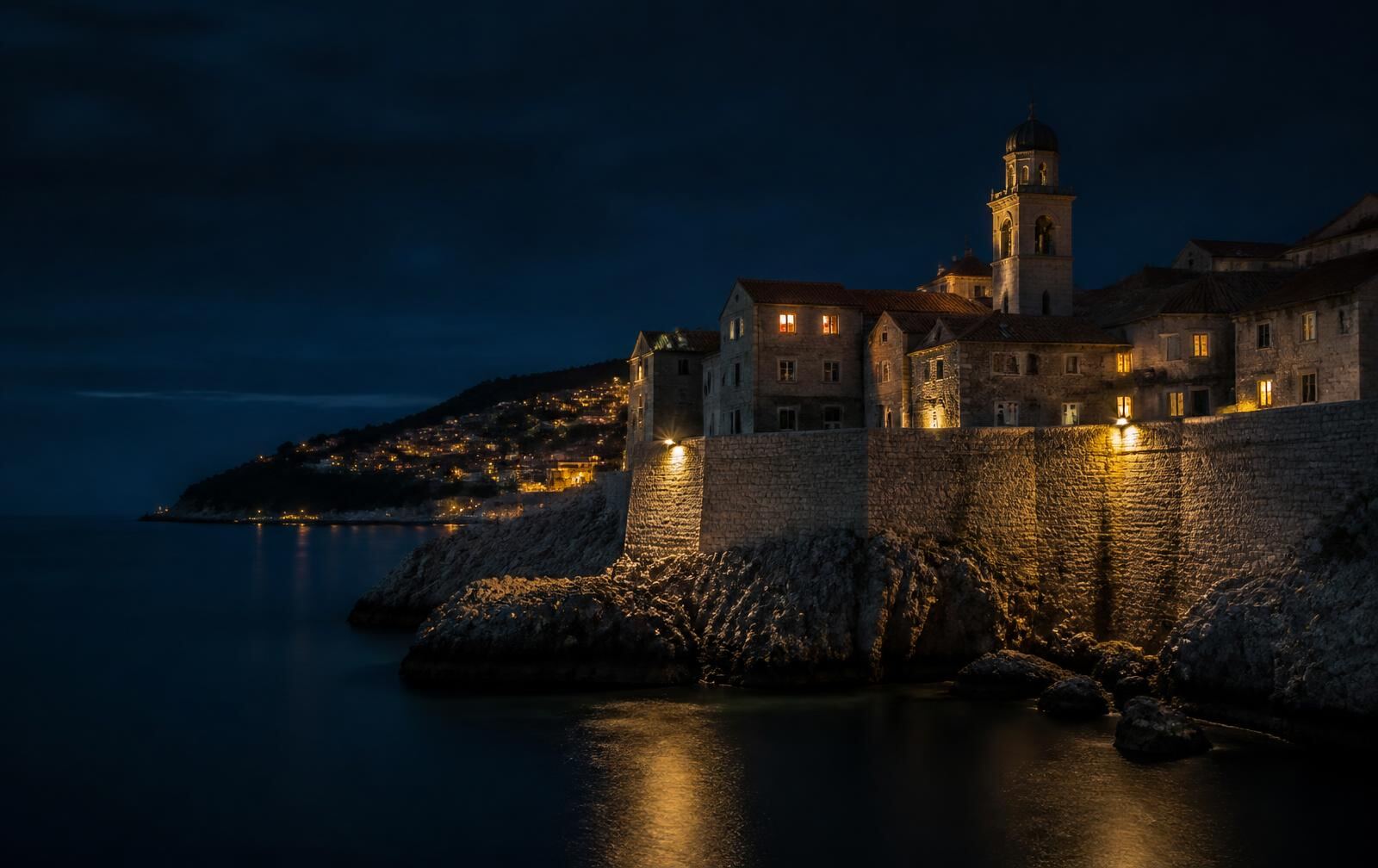 A Croatian coastal town at blue hour — warm waterfront lights along a dark harbour under deepening blue skies