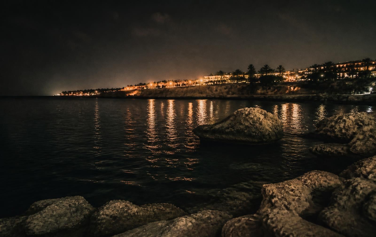 Cyprus coastline at night with warm town lights reflecting on dark Mediterranean water