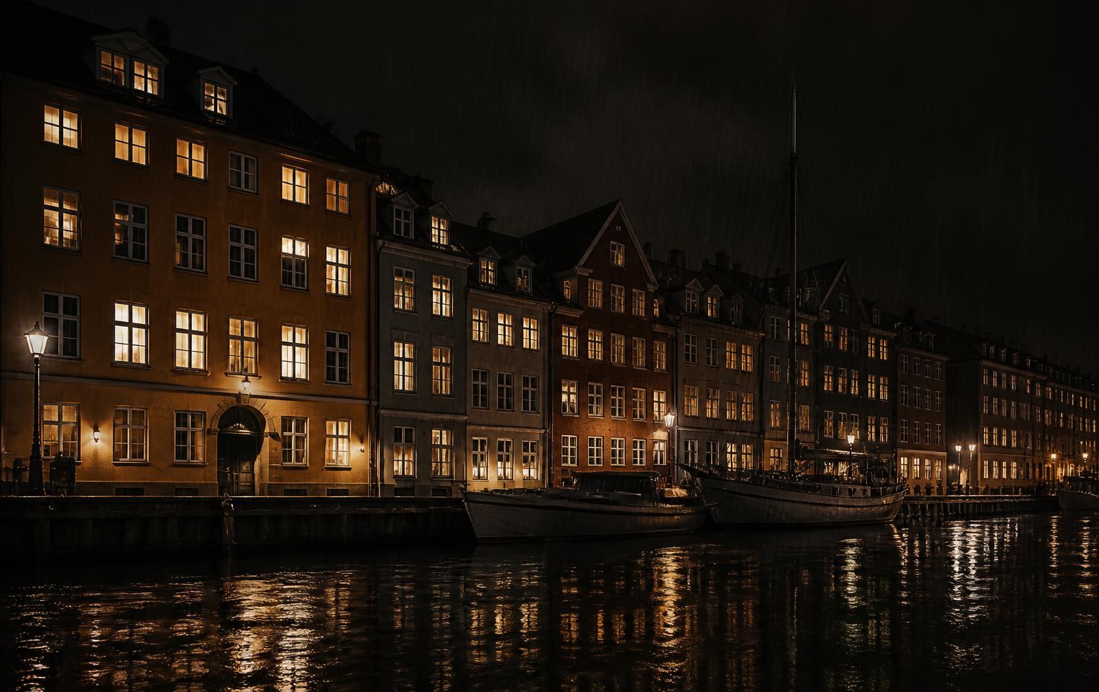 Danish waterfront at night, black water reflecting warm amber light from the windows of low townhouses with rain in the air