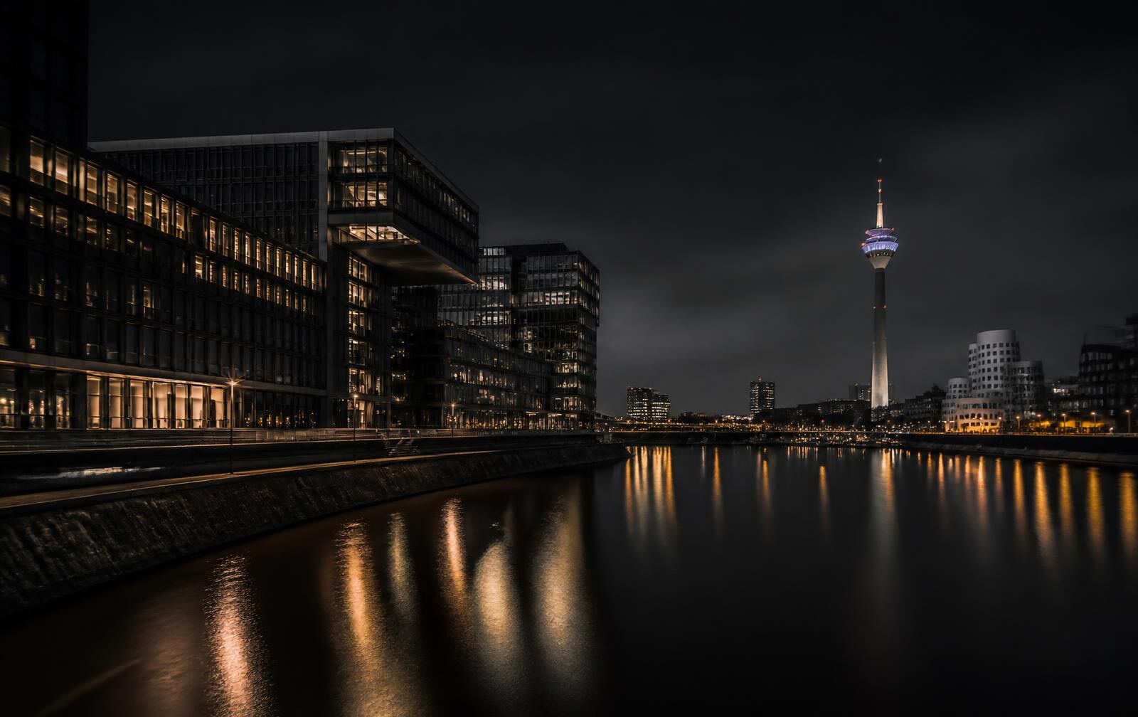 Düsseldorf at night with clean modern architecture along the Rhine and warm gold light reflected on dark water