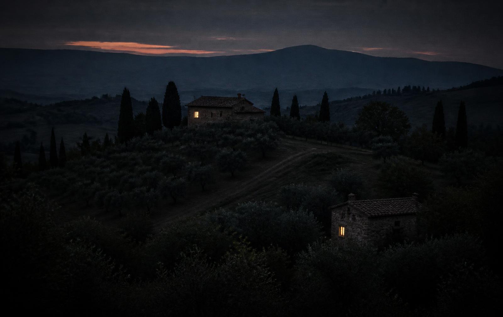 Quiet hills at dusk with two stone houses, a single lit window, cypress trees and layered ridges fading into blue
