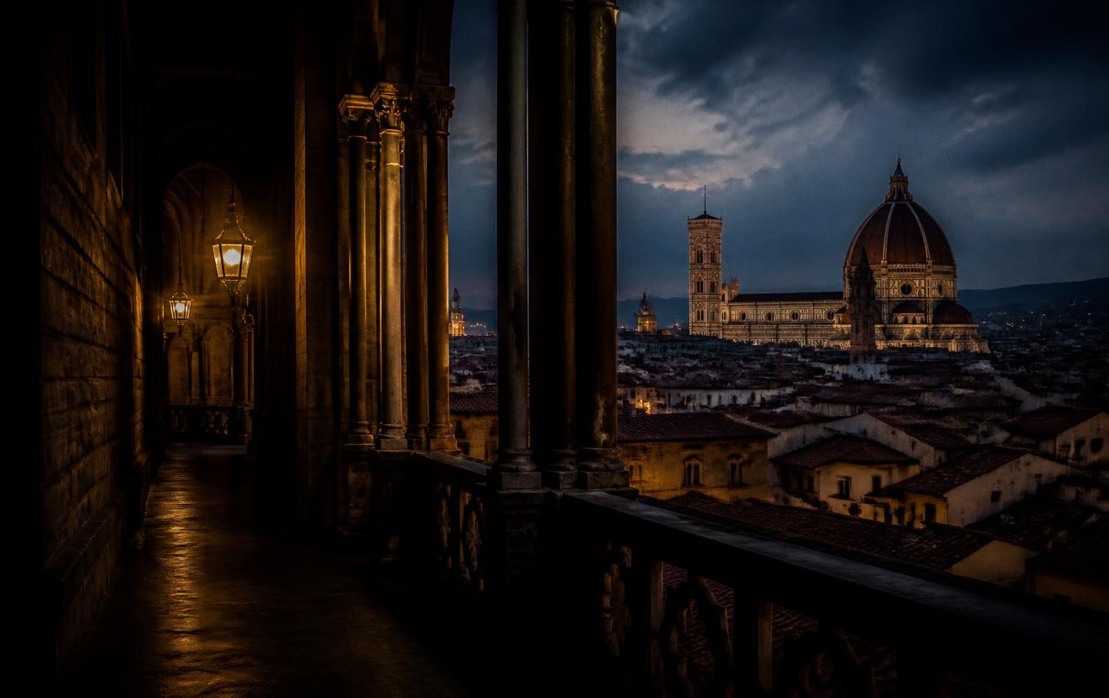A lamplit stone loggia in Florence at dusk looking across terracotta rooftops toward the cathedral dome