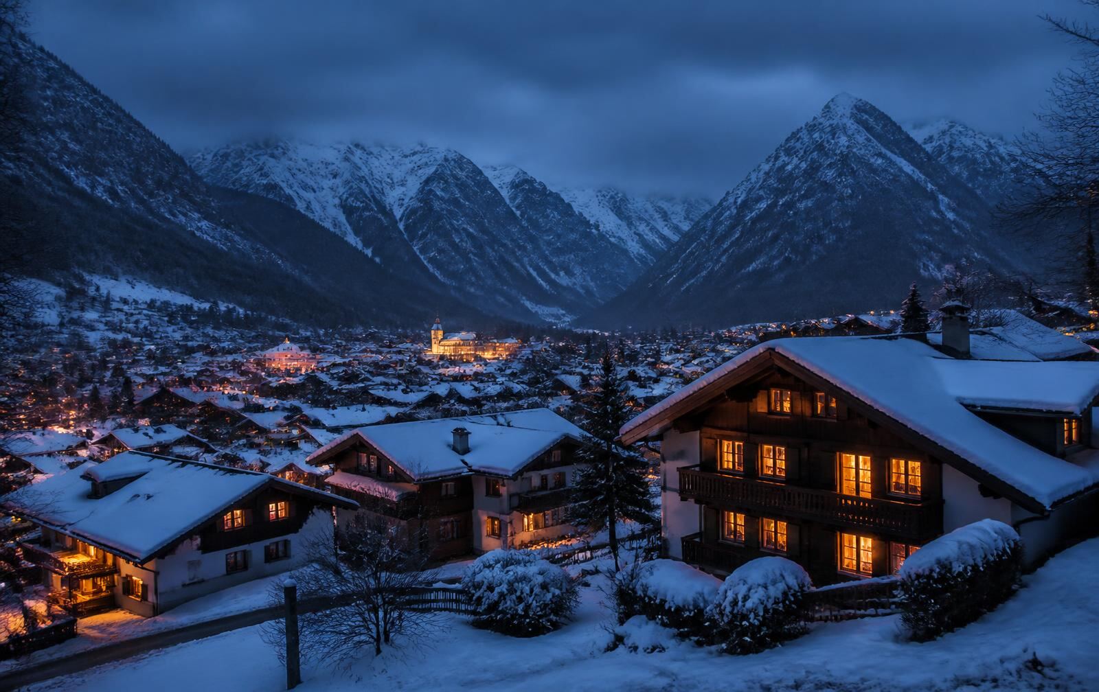 A snow-covered alpine valley town at blue hour with warm lit timber chalet windows and dark mountain ridges behind