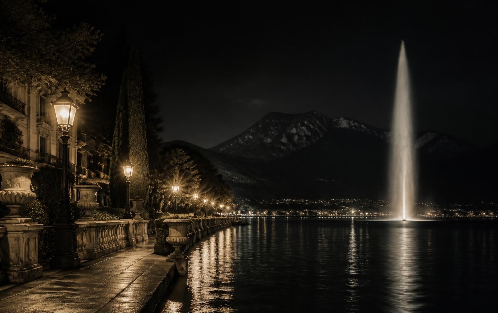 A lakefront promenade in Geneva at night with a tall illuminated water jet and gold lamplight on dark water