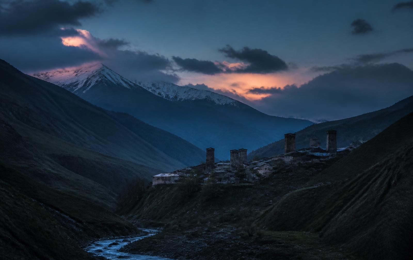 A Georgian old-town evening scene — warm balconies and fortress stone above a dark river gorge