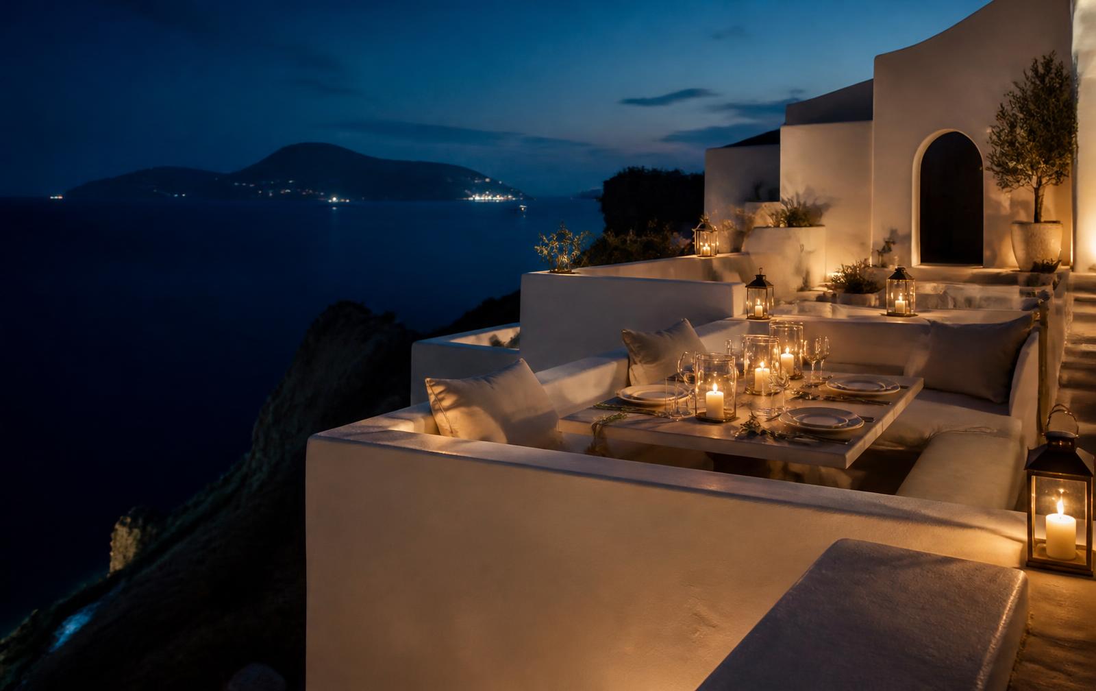 A candlelit white-stone terrace overlooking the Aegean Sea at blue hour