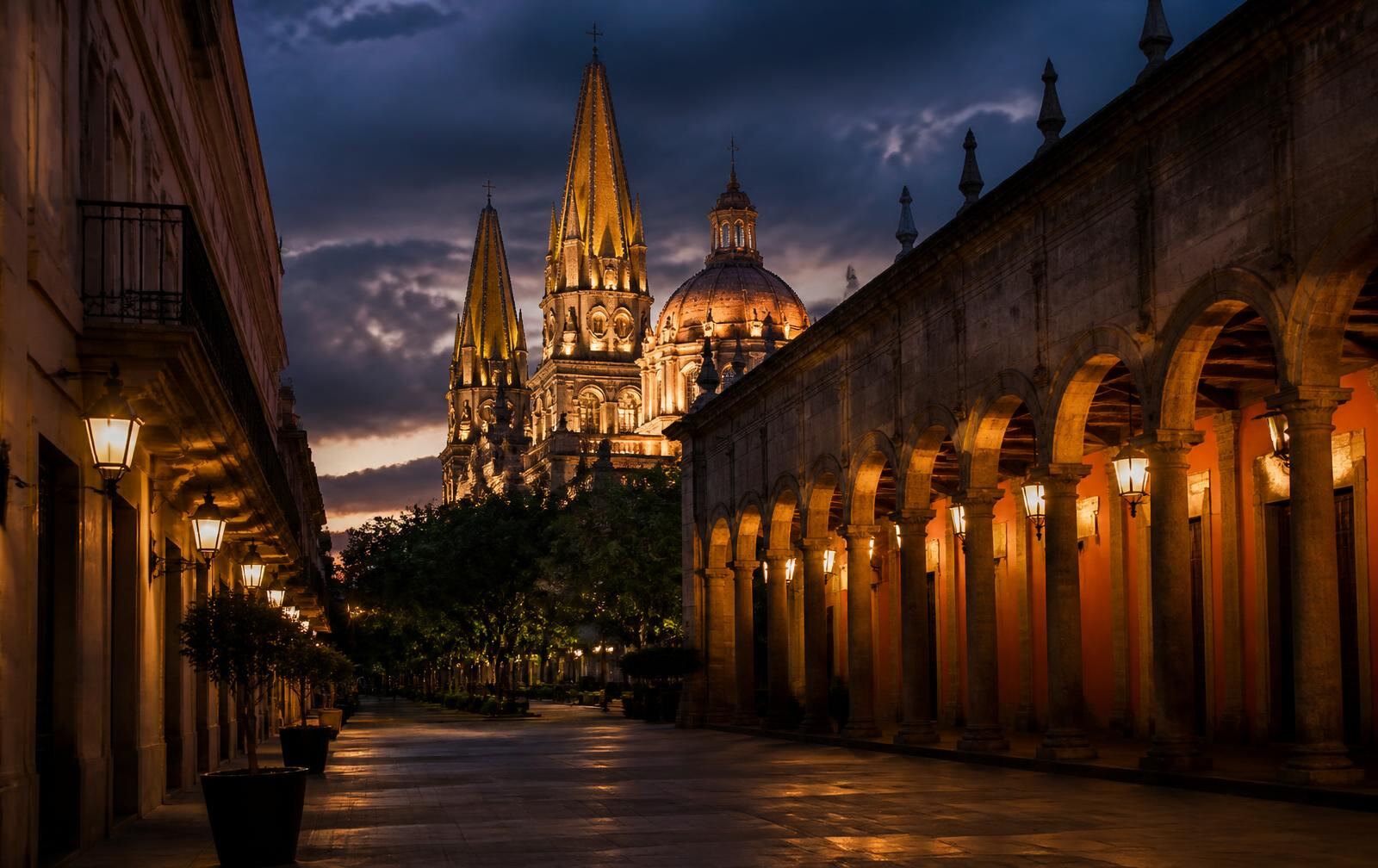 Guadalajara cathedral spires and dome lit at dusk, colonial arcades and lanterns along a quiet plaza