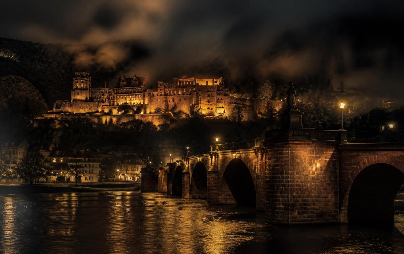 Heidelberg at night with the old bridge and castle above the Neckar, warm lamplight on old stone