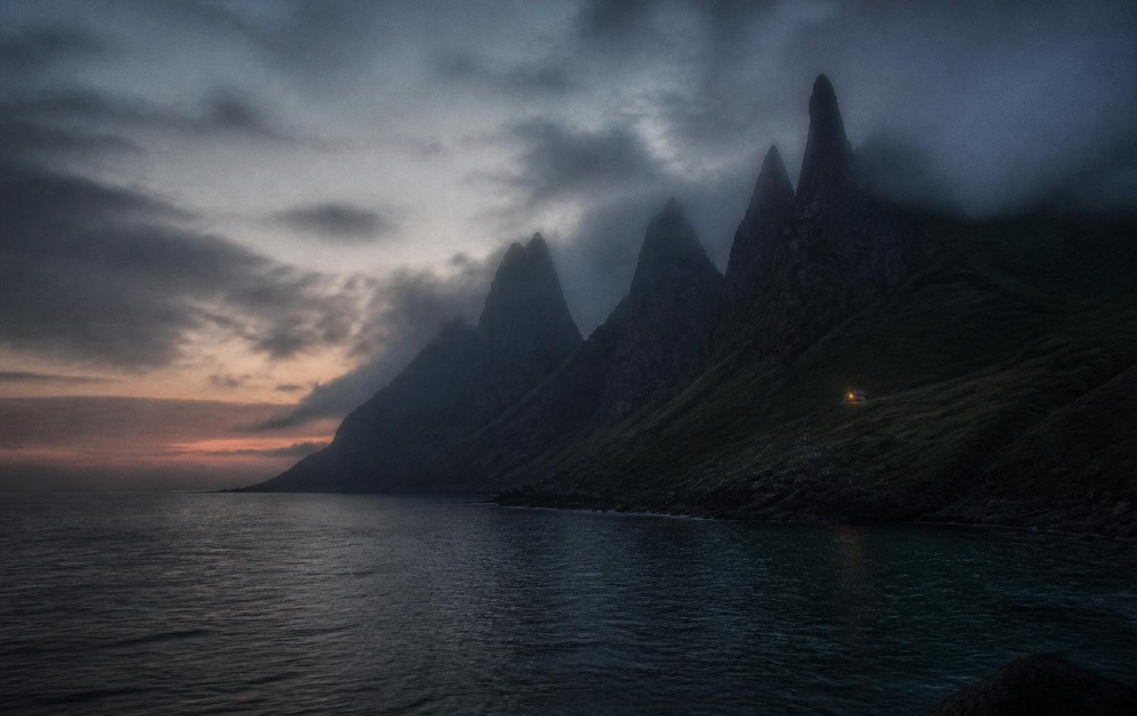 Jagged Isle of Skye ridges in sea mist at dusk above dark water with one distant cottage light