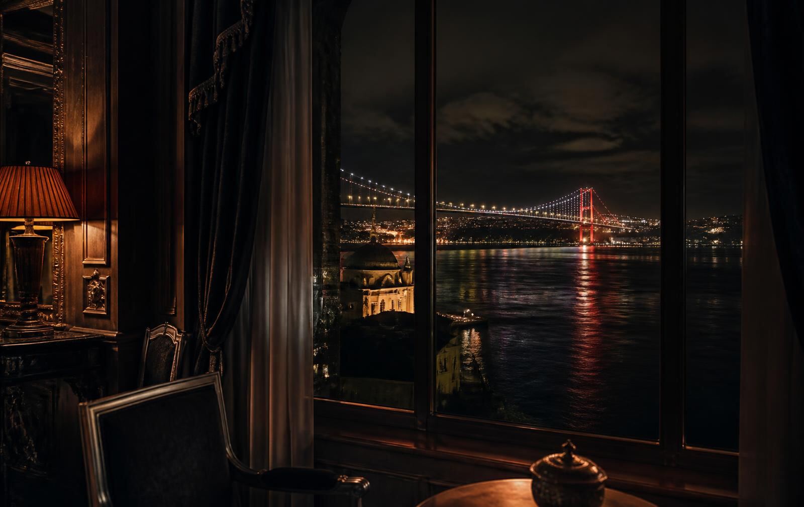 A warmly lit hotel interior with dark wood looking out over the Bosphorus and bridge lights at night