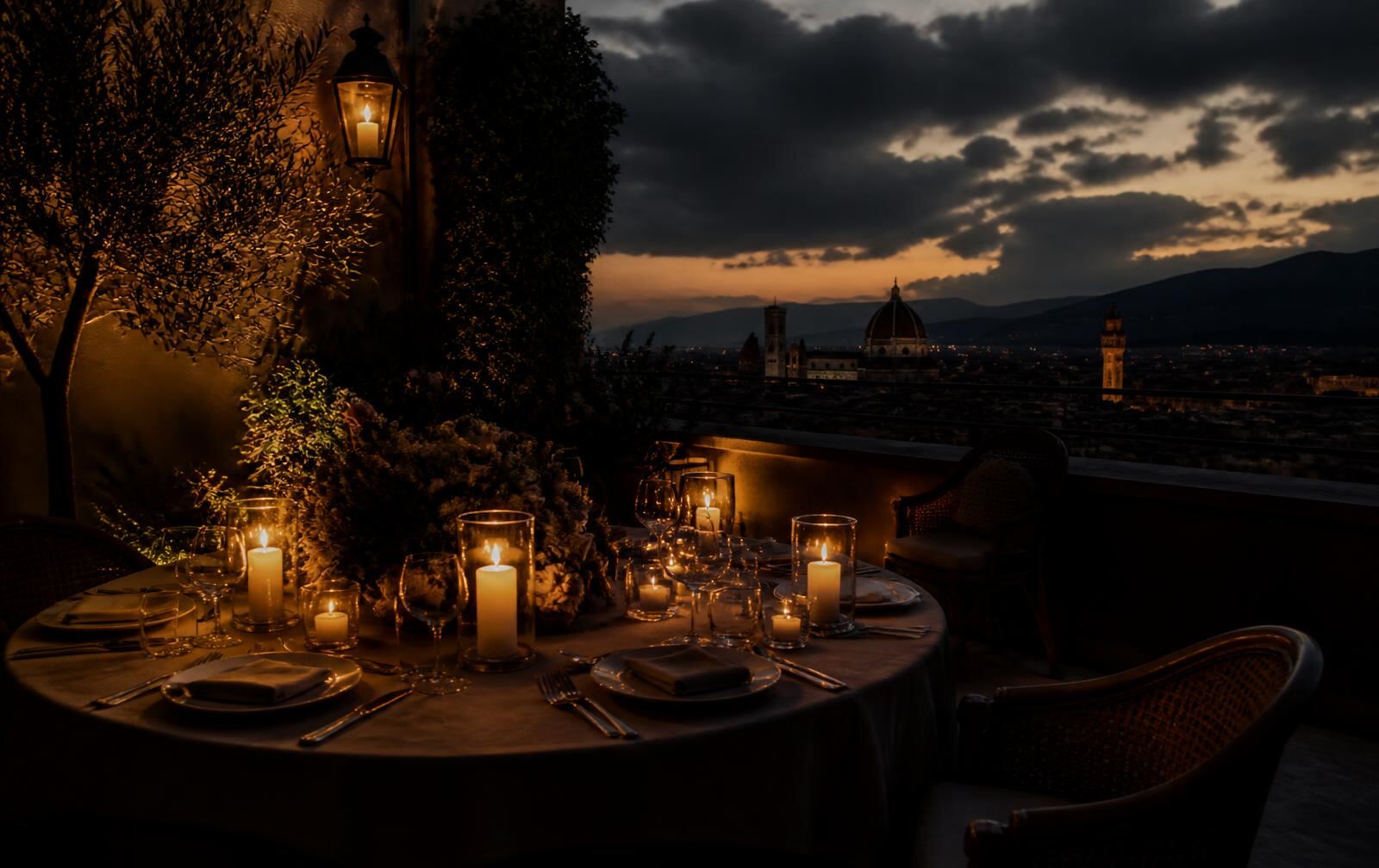 A candlelit Italian terrace at dusk overlooking a lamplit city and distant hills