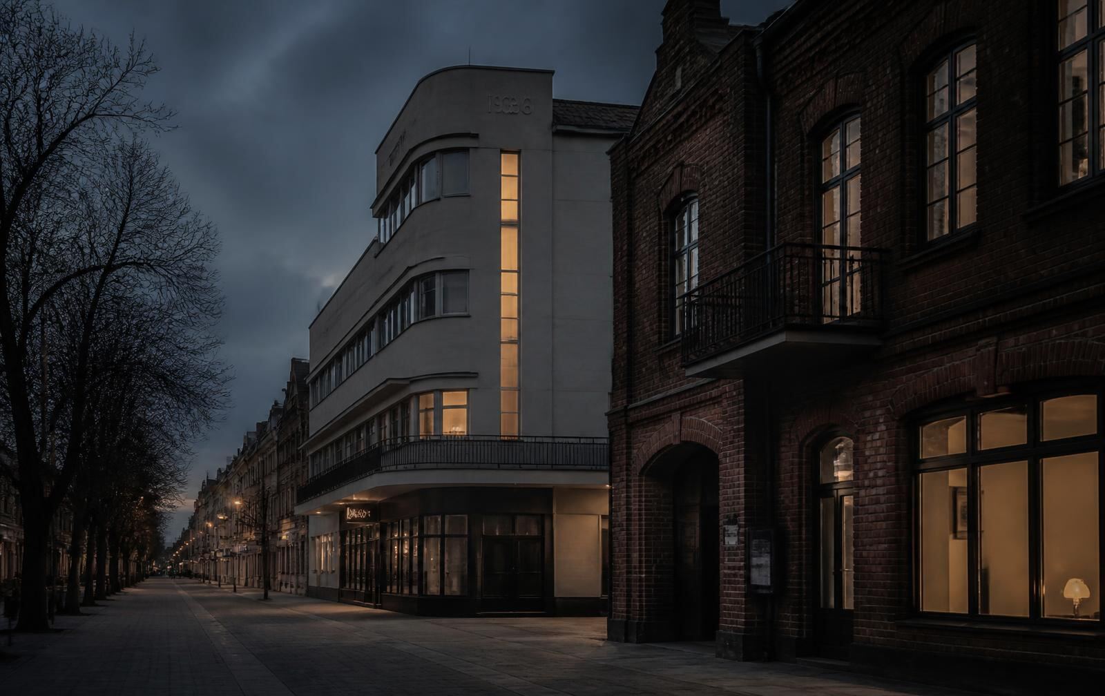 Kaunas street at dusk with a white 1930s modernist corner building beside older brick facades, warm lit windows and an empty tree-lined avenue