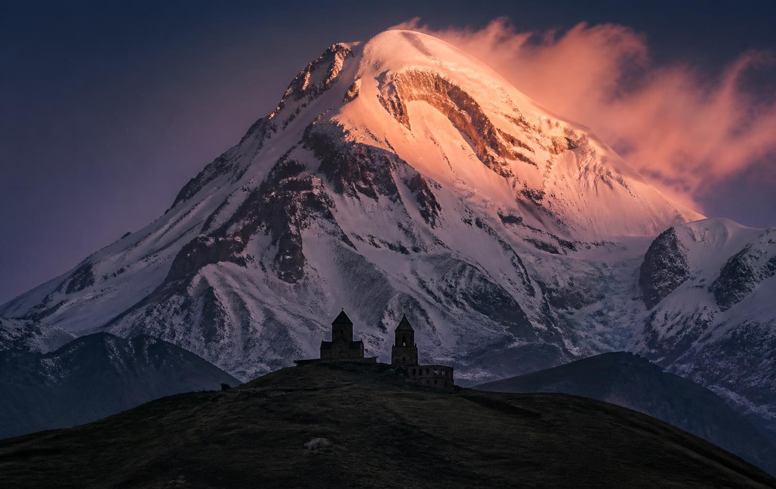 Gergeti Trinity Church silhouetted beneath the snow face of Mount Kazbek at dusk