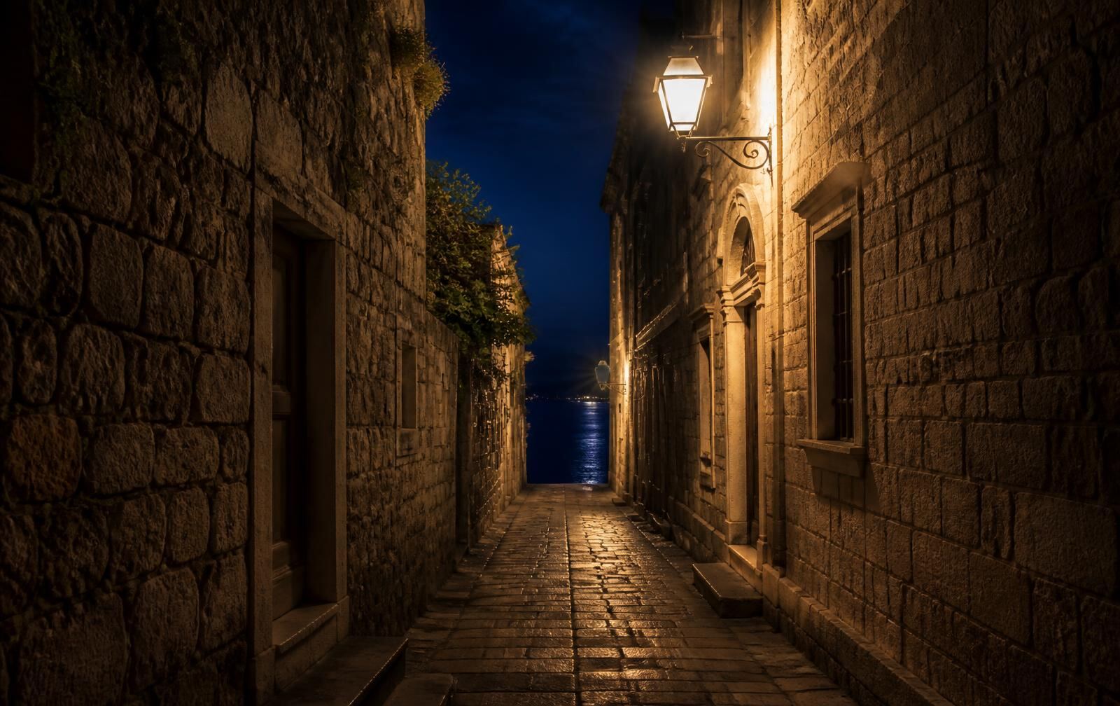 A lantern-lit stone lane in Korčula's old town at night, ending in a glimpse of dark sea