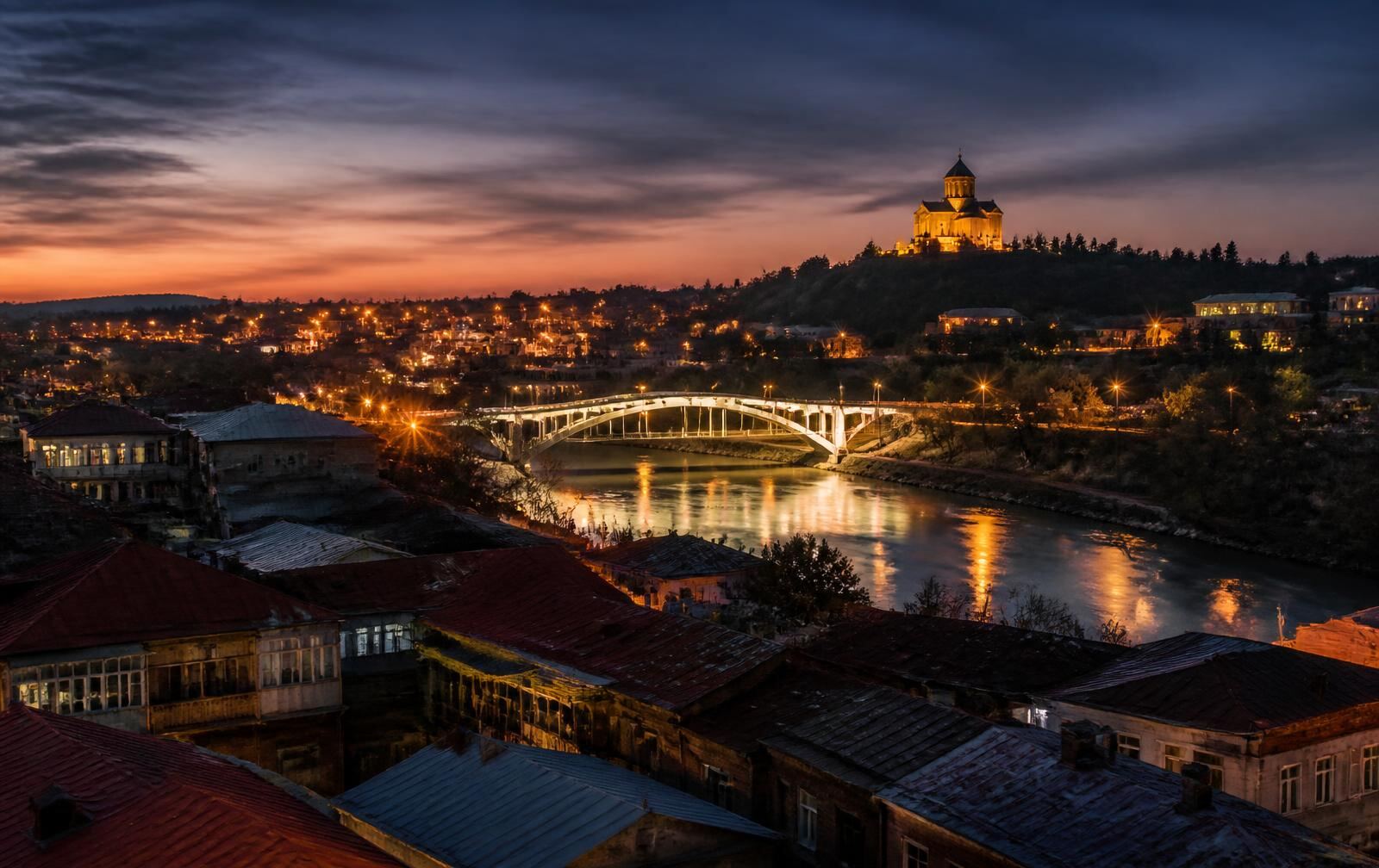 Kutaisi at dusk, the white bridge over the Rioni river and Bagrati Cathedral lit on the hill above old rooftops
