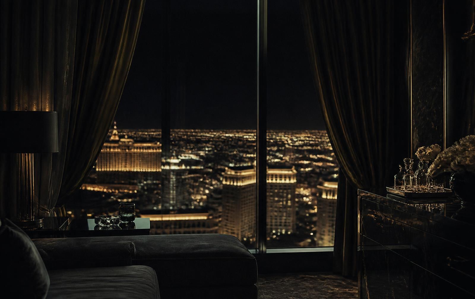High hotel suite window overlooking the glowing Las Vegas Strip at night, the room itself dim and still
