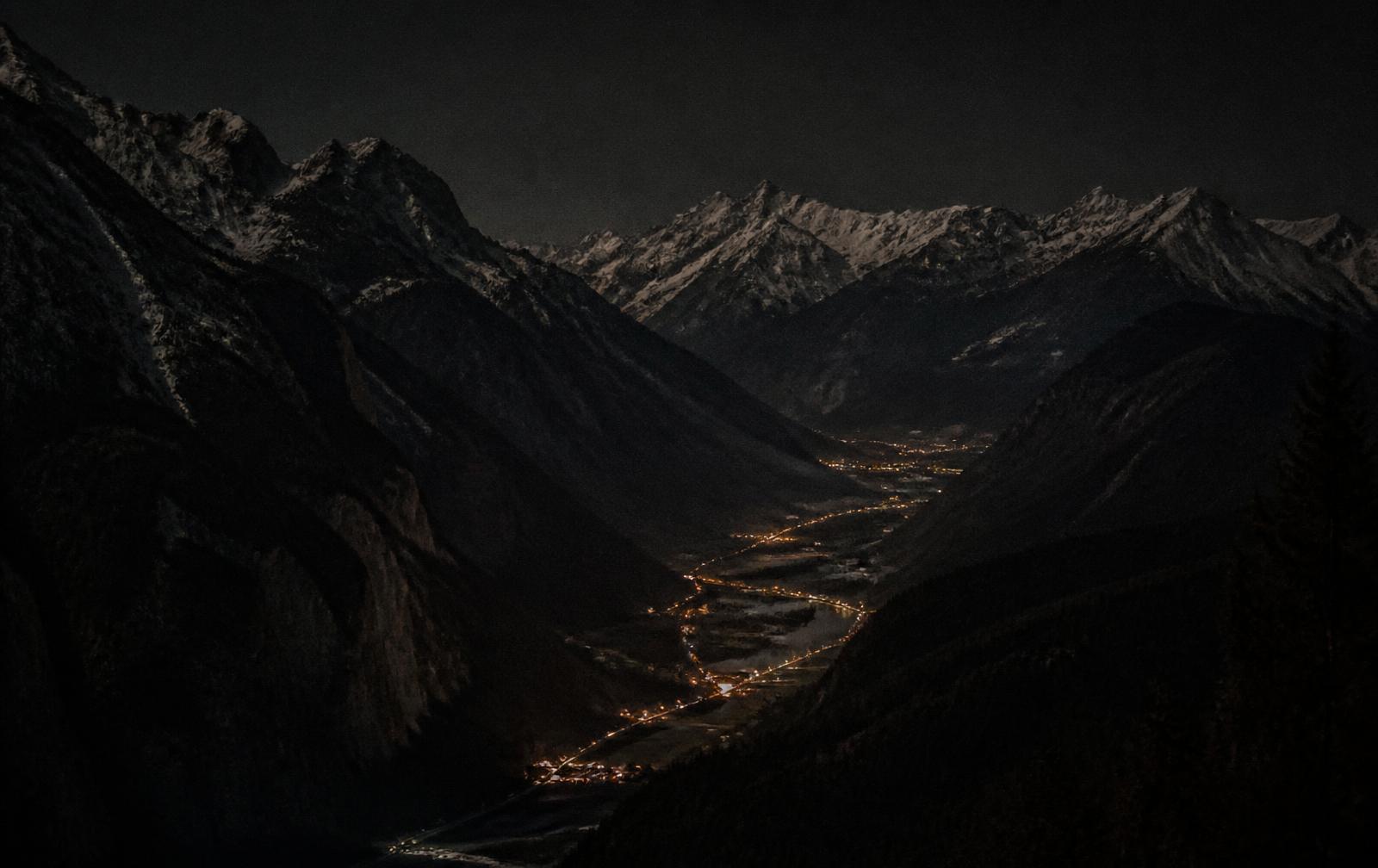 An alpine valley at night with scattered amber village lights beneath dark mountain ridges