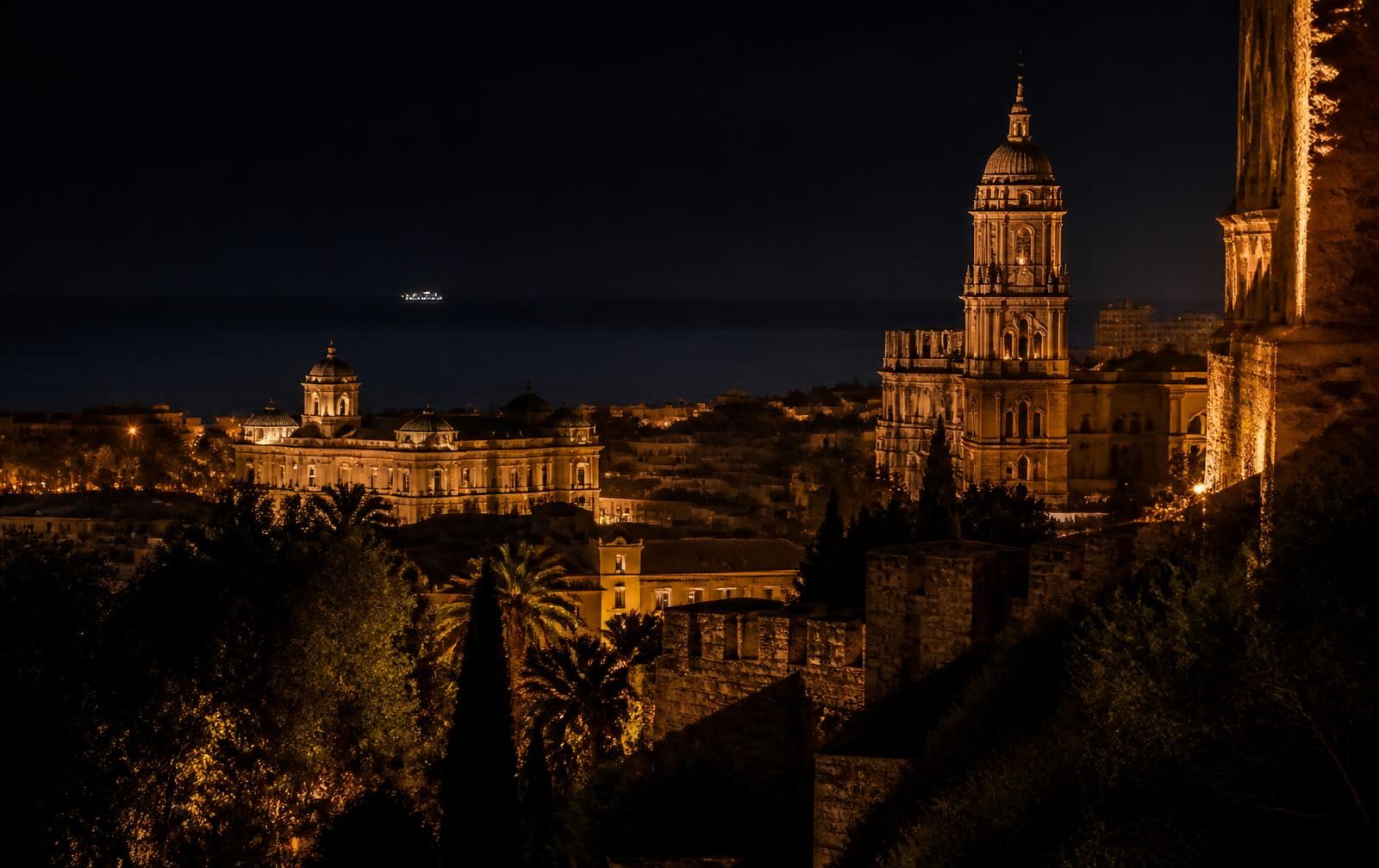 Málaga old town at night with warm gold light on Andalusian stone architecture above a dark sea