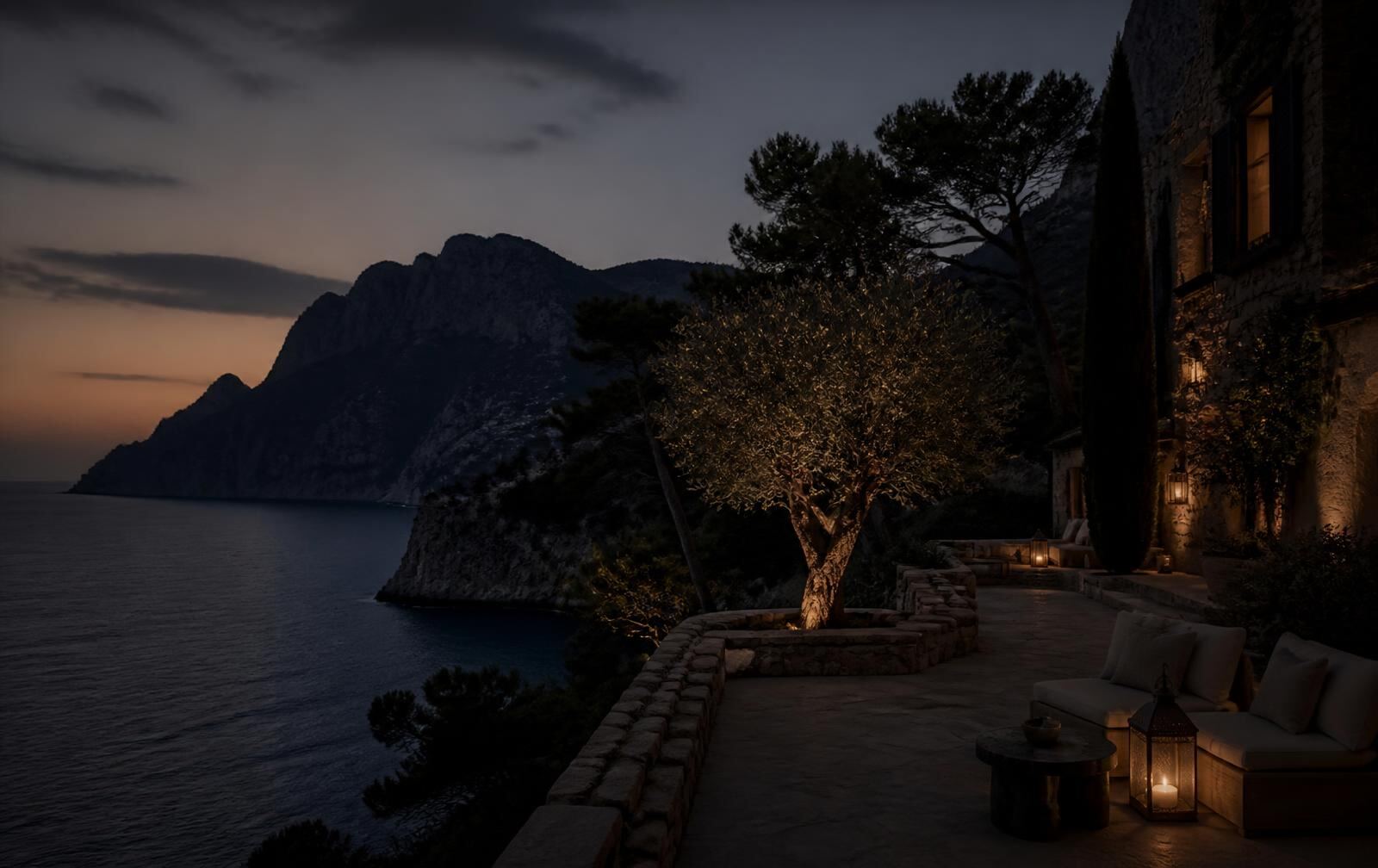 A lantern-lit Mallorca villa terrace at dusk above a dark sea with Tramuntana cliffs behind