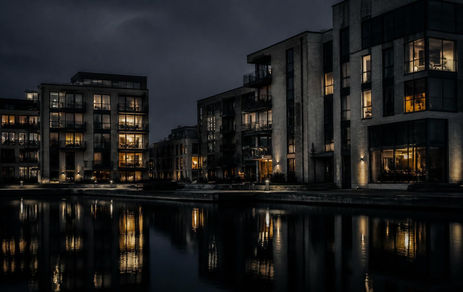 A modern southern Swedish waterfront district at night, contemporary buildings with warm lit windows reflected in a still dark canal basin