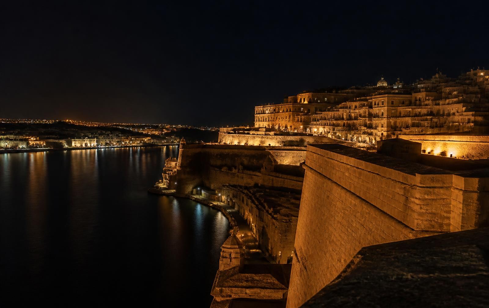 Limestone bastions above a great natural harbour at night with warm amber lights reflected in dark water