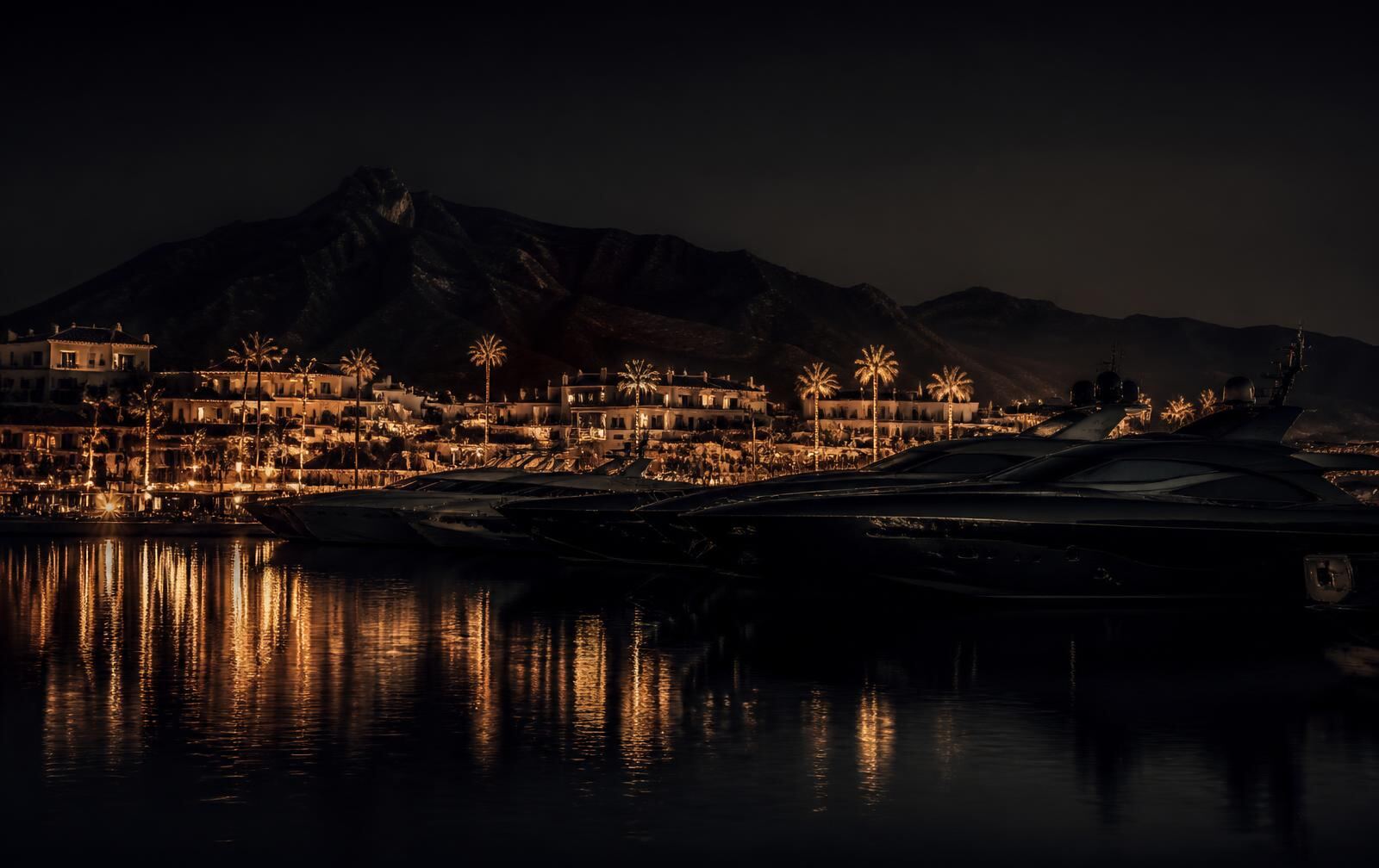 A luxury Marbella marina at night with yacht silhouettes and warm gold lights reflected on dark water