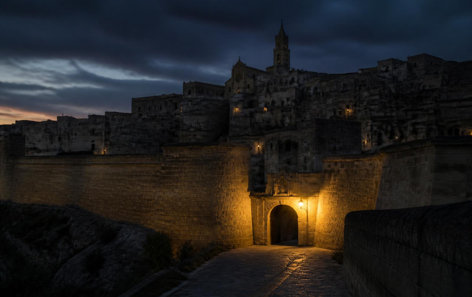 A walled hilltop town at dusk with honey limestone bastions and a single warmly lit arched gateway