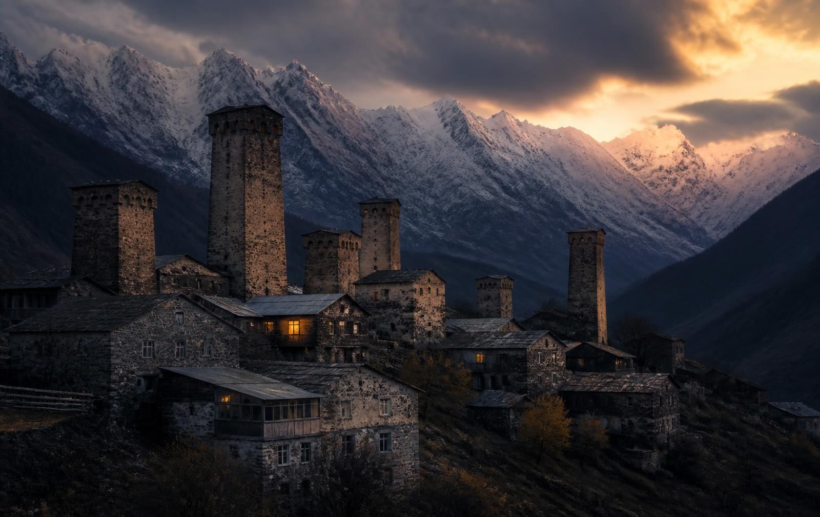 Mestia in Svaneti at dusk, medieval stone watchtowers of a mountain village under snow peaks with a few warm windows