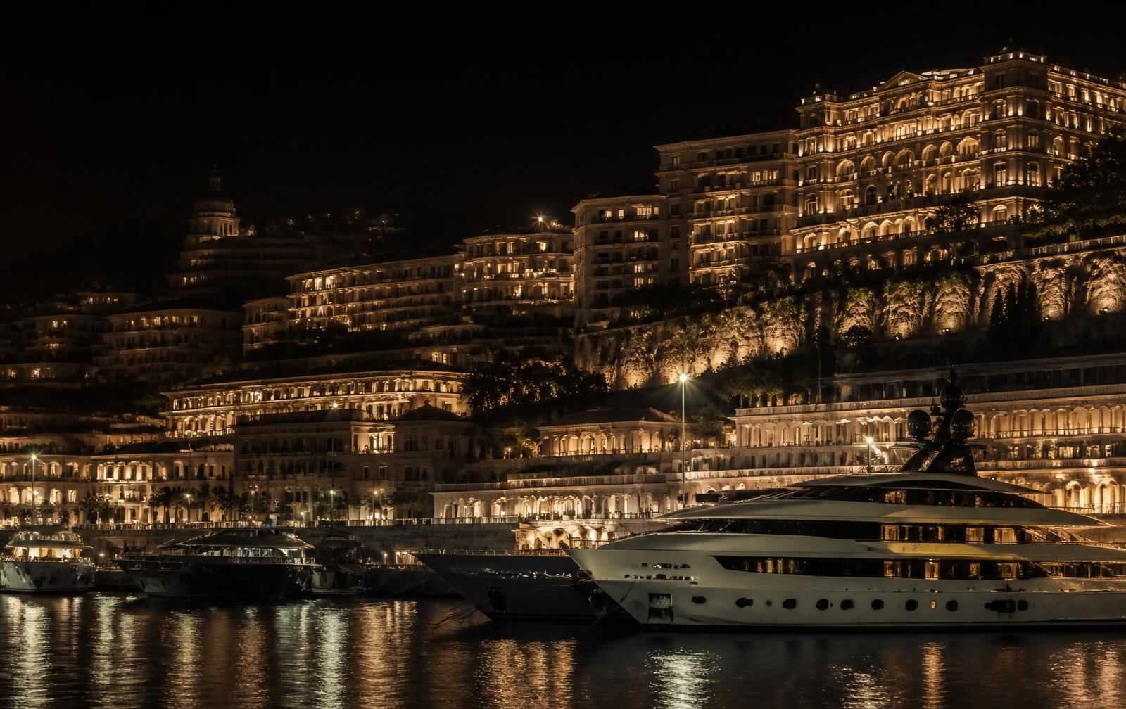 Yachts moored beneath warmly lit cliffside architecture in Monaco at night