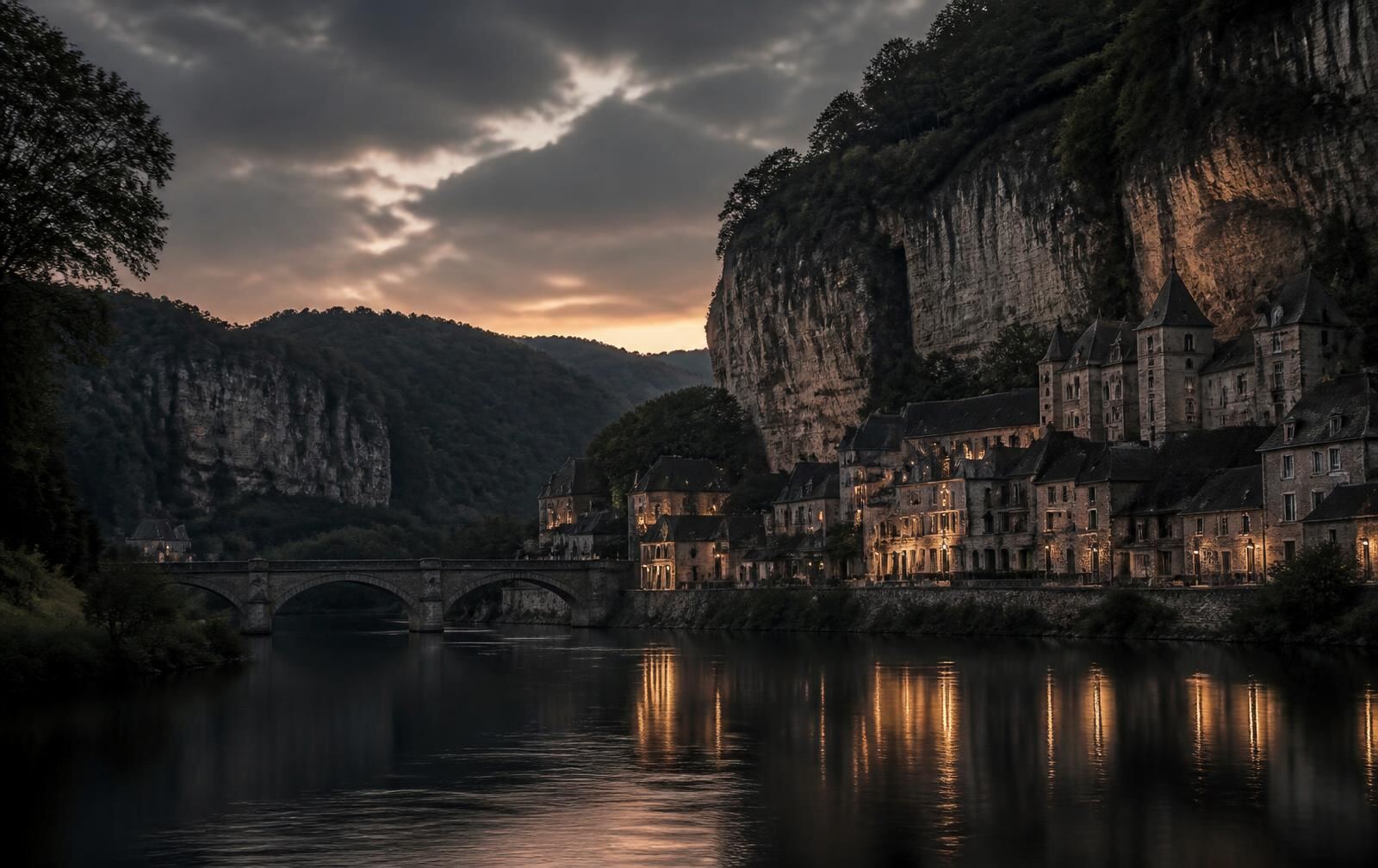 Broad Meuse river at dusk between wooded limestone cliffs with an old stone town of lit slate-roofed houses along the water