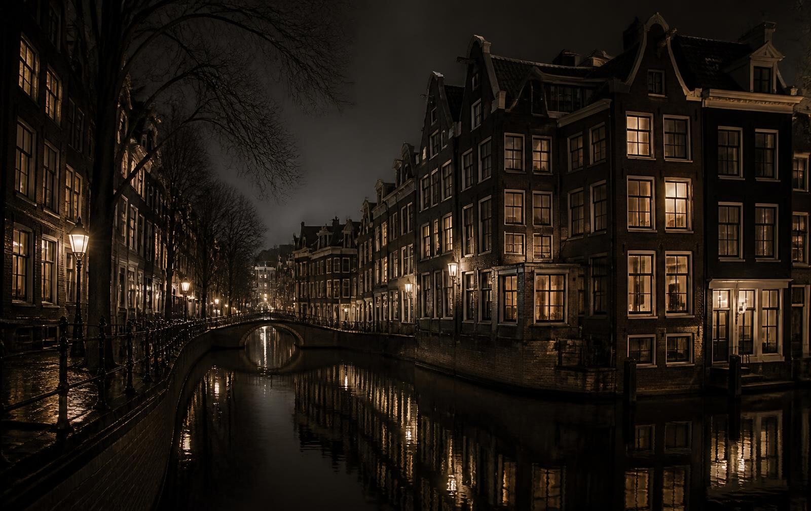 Rain-wet Dutch canal at night with historic canal houses, warm lit windows and an arched bridge reflected in dark water