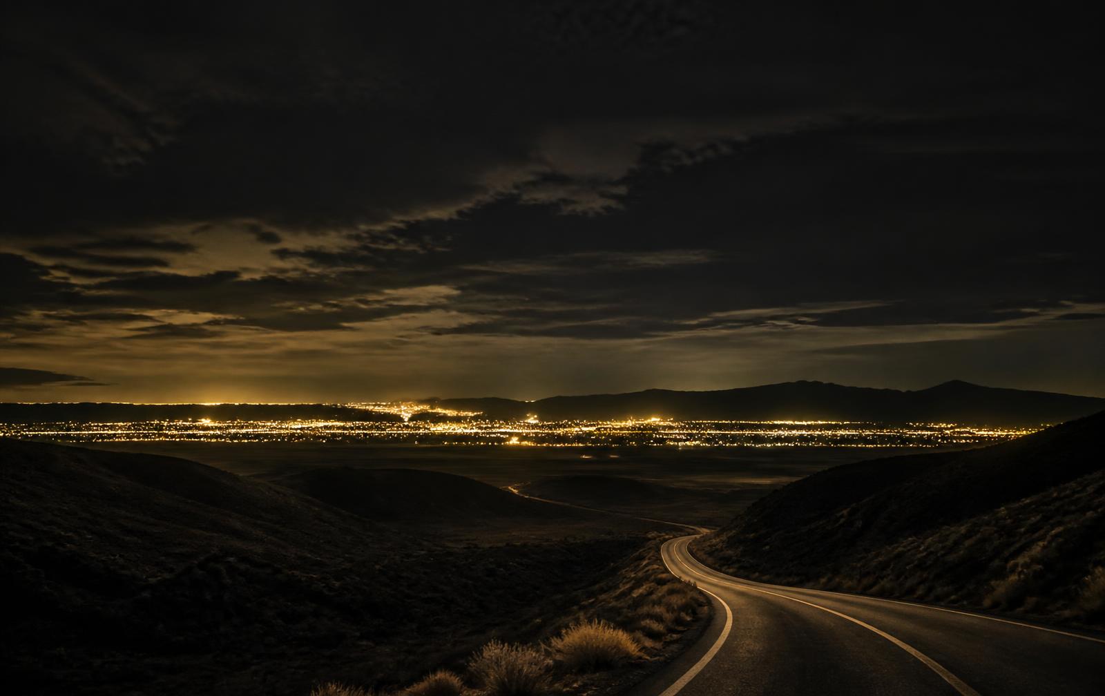 Desert horizon at dusk with distant city lights beginning to glow beneath a darkening sky