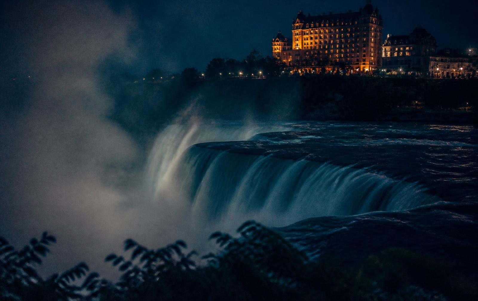 Night mist above dark falling water with distant warm hotel lights along the Niagara gorge