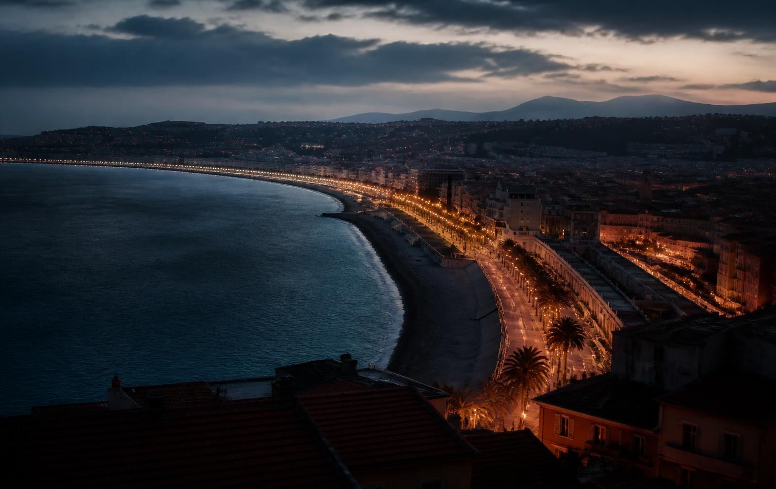 The bay of Nice at blue hour with a lamplit curving promenade and old town rooftops