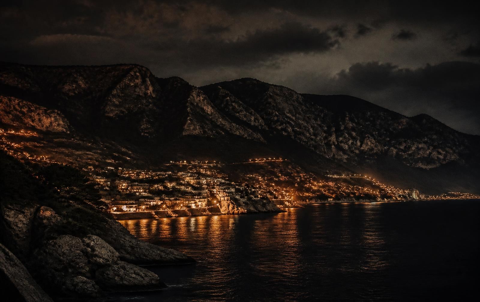 Northern Cyprus coastline at night with a dark mountain ridge and scattered warm town lights above the sea