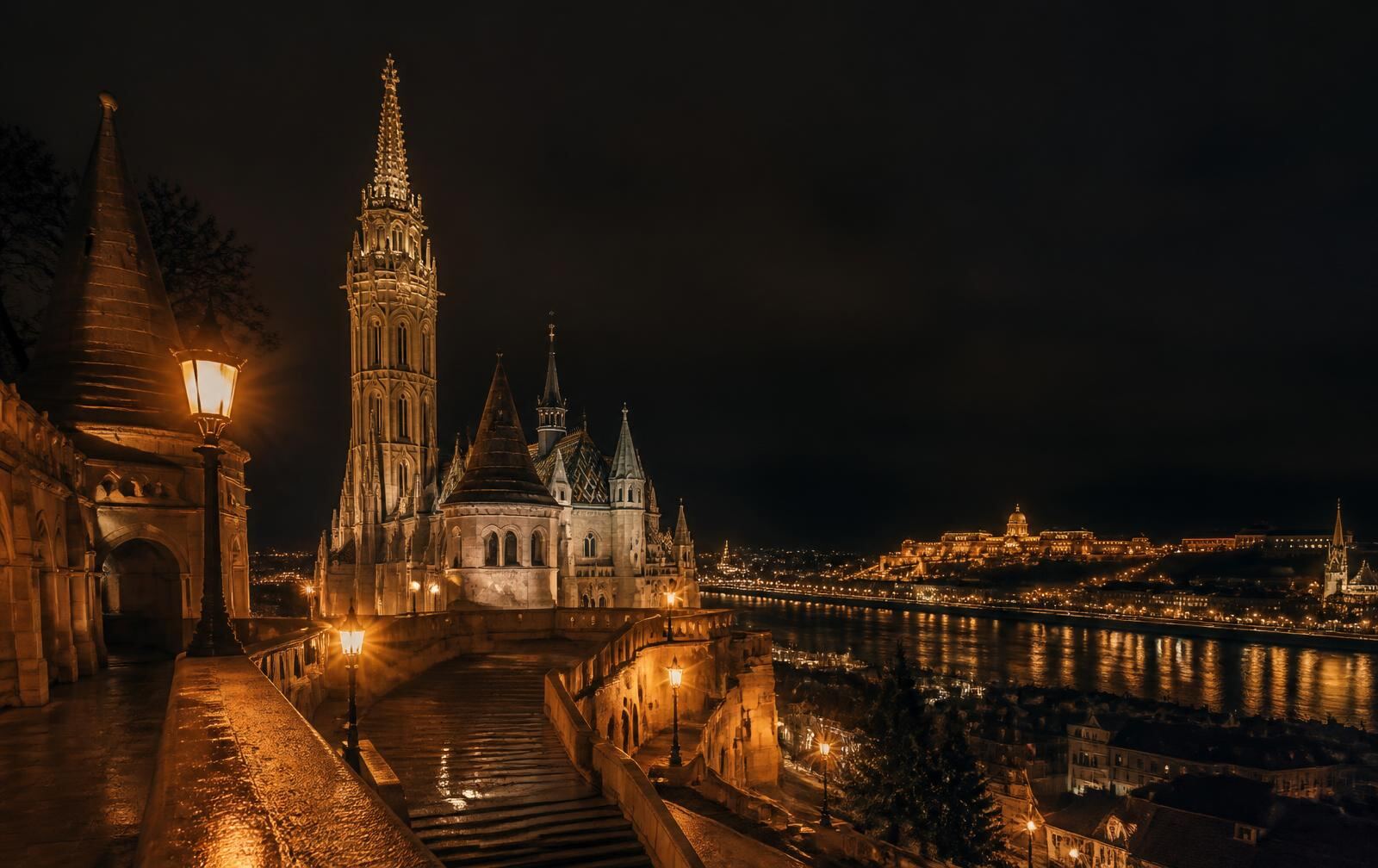 An elegant Central European city at night with a lit cathedral spire and a fortress above the Danube