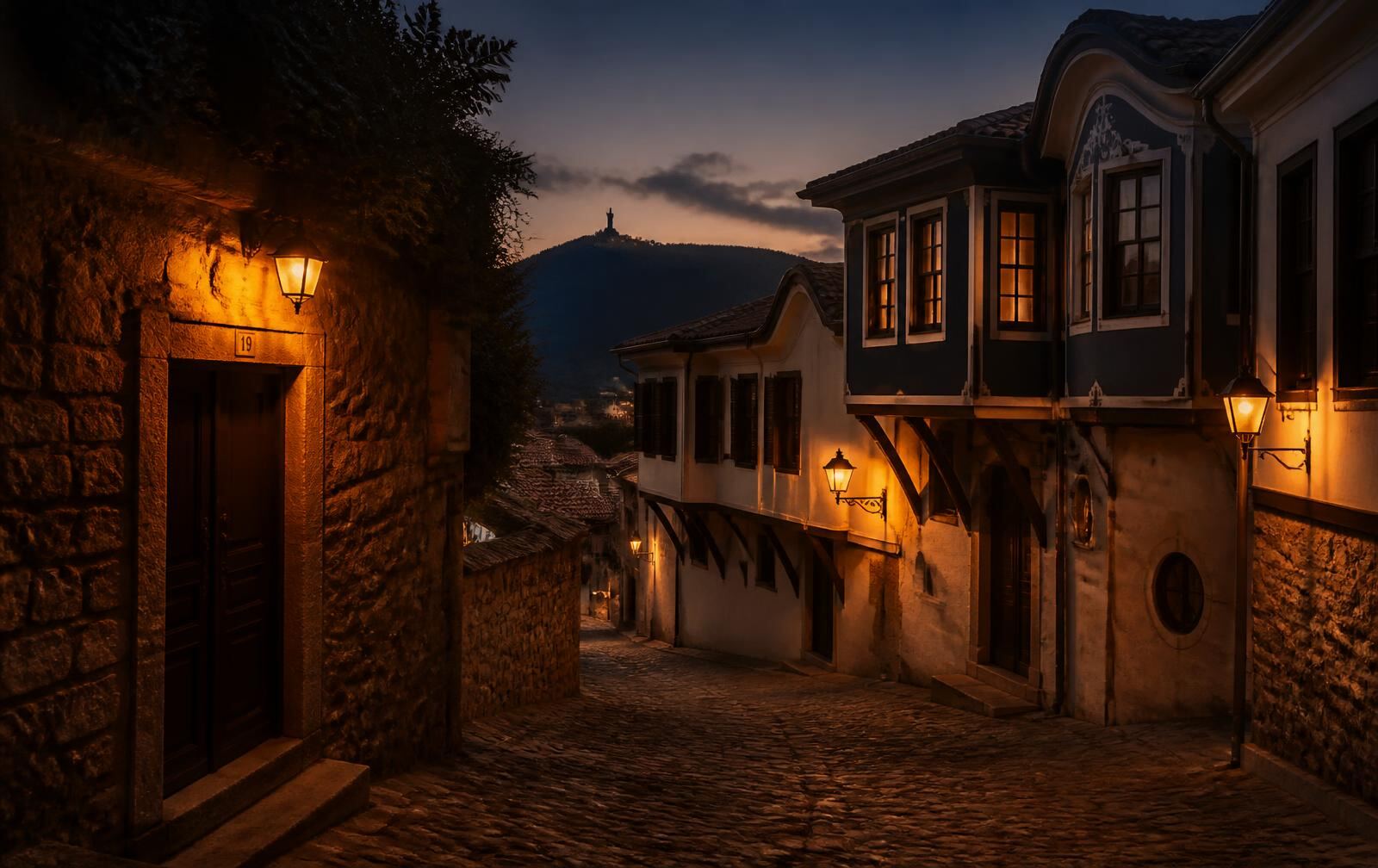 Plovdiv's old town at dusk — lantern-lit cobbled lane between Revival-era houses under a dark hill